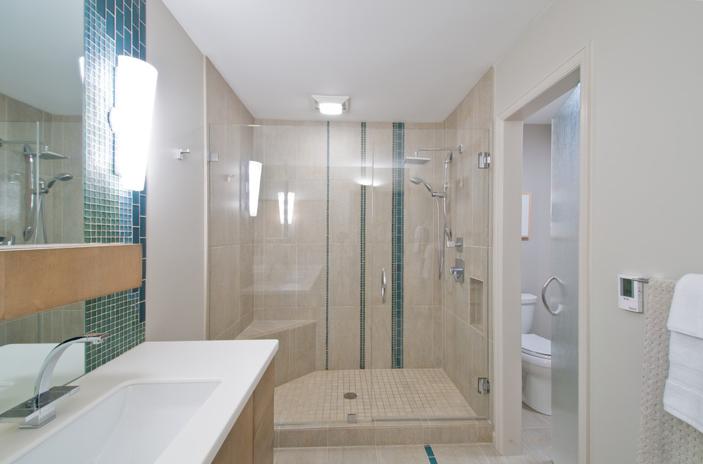 Inspiration for a mid-sized transitional master bathroom in Detroit with flat-panel cabinets, light wood cabinets, an alcove shower, a two-piece toilet, beige tile, glass tile, beige walls, porcelain floors, an integrated sink, solid surface benchtops, beige floor and a hinged shower door.