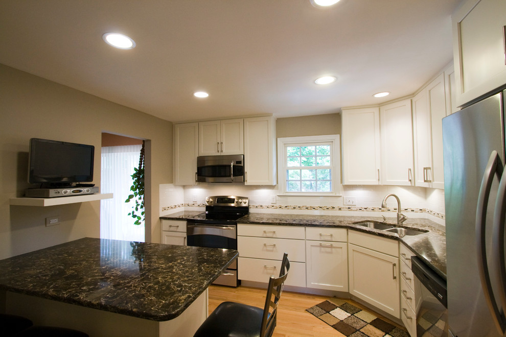 Example of a large transitional l-shaped light wood floor enclosed kitchen design in DC Metro with an undermount sink, shaker cabinets, white cabinets, granite countertops, white backsplash, subway tile backsplash, stainless steel appliances and an island