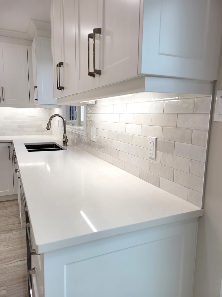 Example of a huge transitional u-shaped vinyl floor eat-in kitchen design with an undermount sink, white cabinets, quartzite countertops, gray backsplash, stone tile backsplash, stainless steel appliances, an island and white countertops
