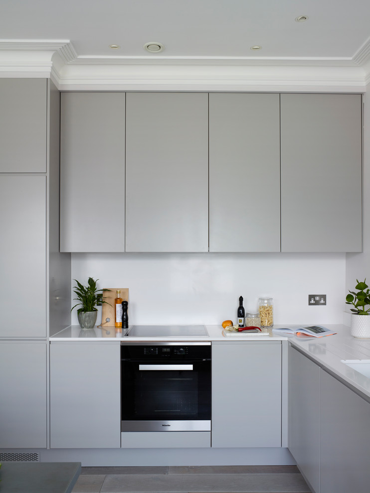 This is an example of a large contemporary l-shaped eat-in kitchen in London with flat-panel cabinets, grey cabinets, solid surface benchtops, yellow splashback, no island and white benchtop.