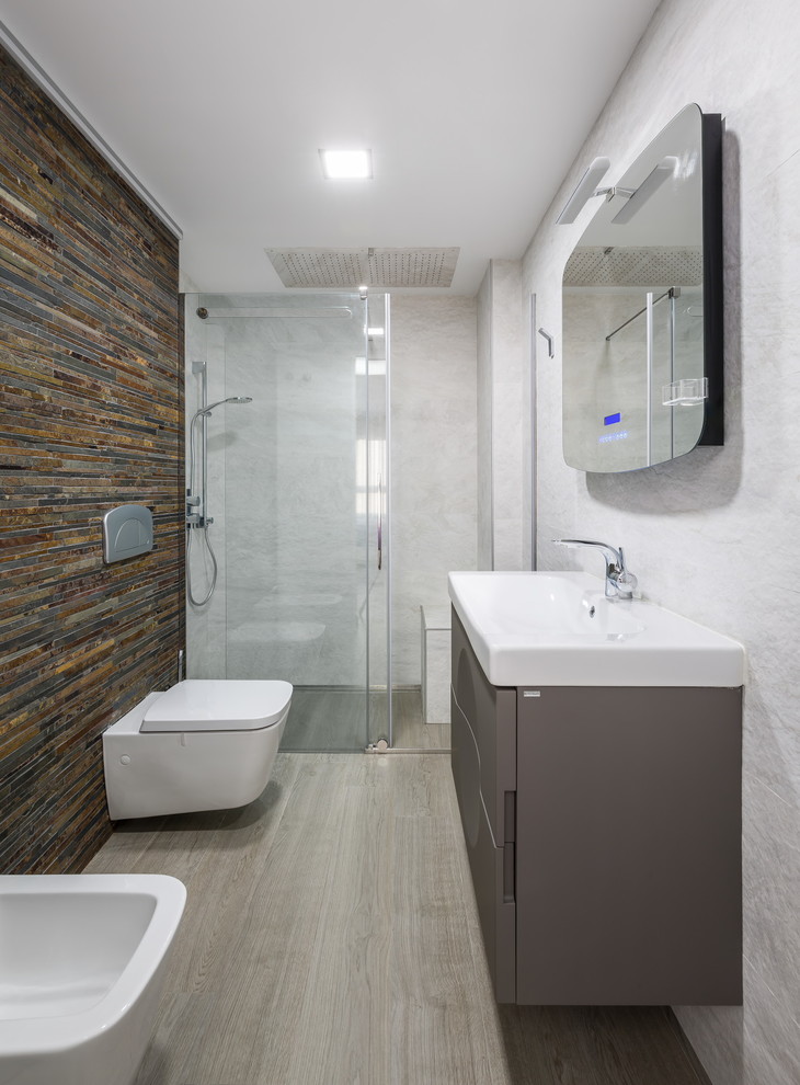 Small contemporary 3/4 bathroom in Valencia with an alcove shower, a wall-mount toilet, brown tile, stone tile, brown walls, a trough sink, flat-panel cabinets and grey cabinets.