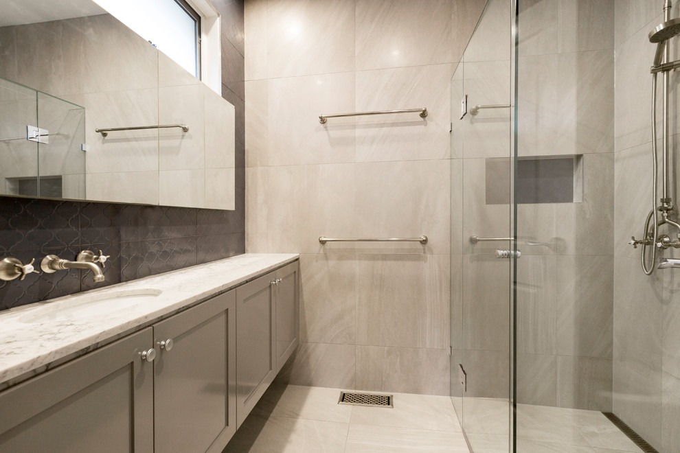 Photo of a mid-sized contemporary bathroom in Melbourne with beaded inset cabinets, grey cabinets, an alcove shower, beige tile, black tile, travertine, beige walls, travertine floors, a drop-in sink and marble benchtops.
