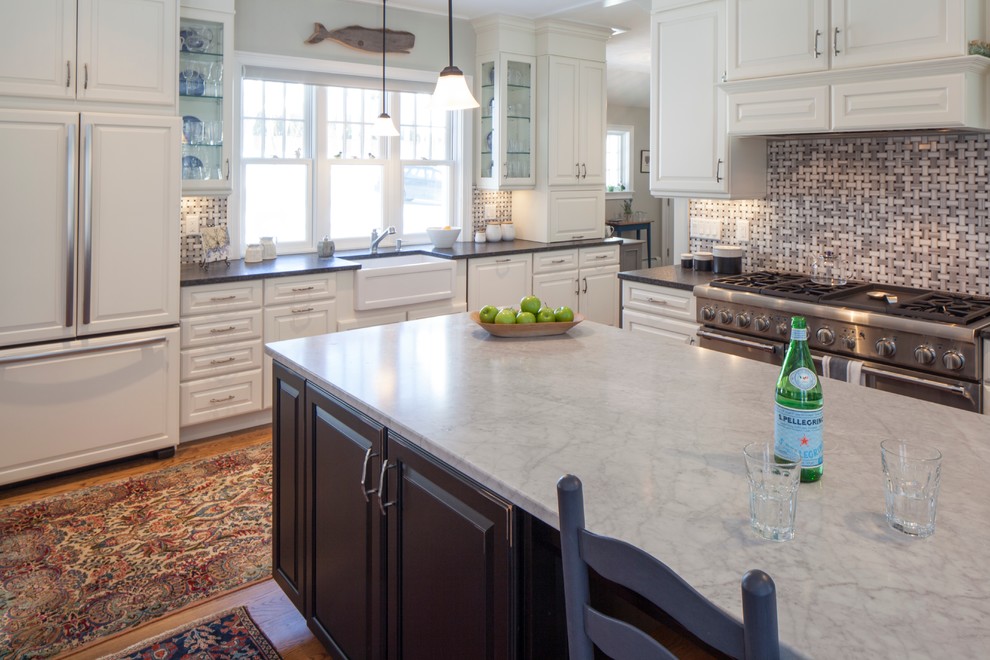 This is an example of a mid-sized country l-shaped open plan kitchen in Portland Maine with a farmhouse sink, raised-panel cabinets, white cabinets, marble benchtops, beige splashback, glass tile splashback, stainless steel appliances, medium hardwood floors and with island.