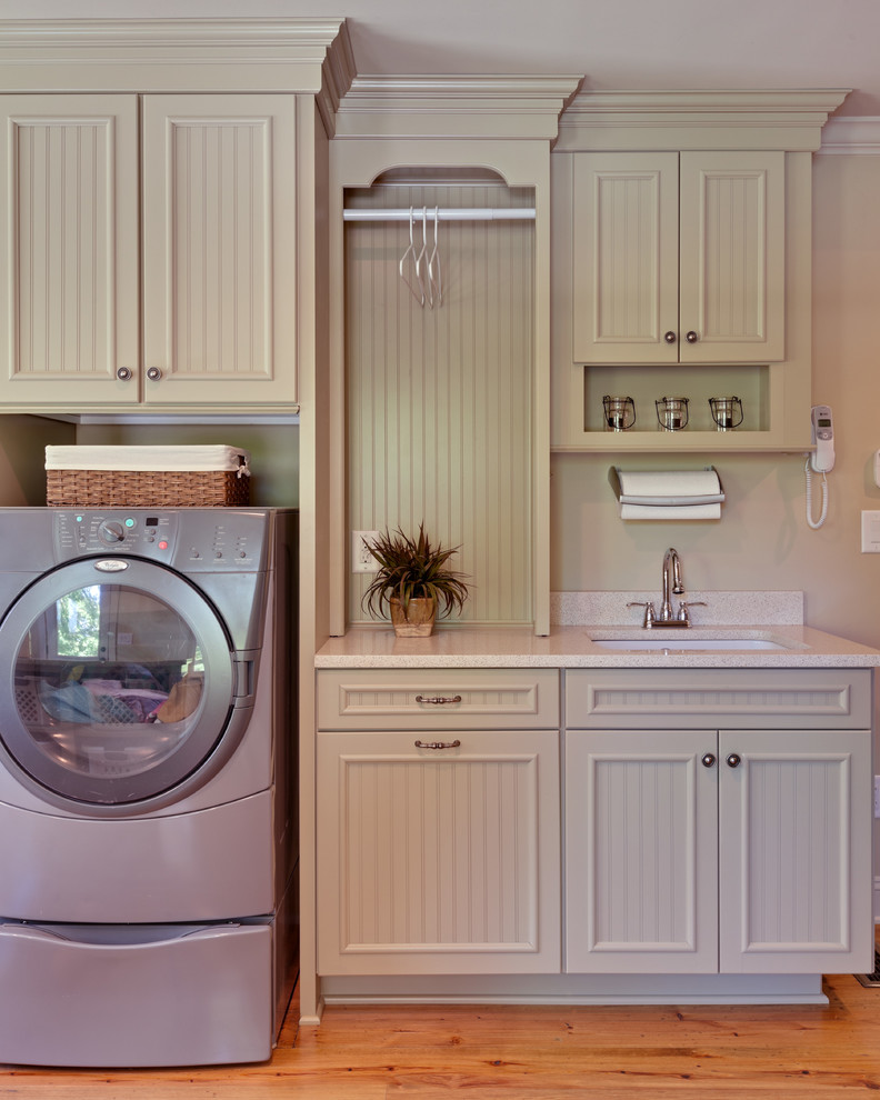 Design ideas for an expansive country u-shaped dedicated laundry room in Atlanta with an undermount sink, green cabinets, quartz benchtops, beige walls, medium hardwood floors, a side-by-side washer and dryer, recessed-panel cabinets, brown floor and white benchtop.