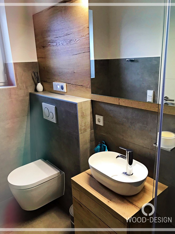 Kleine Moderne Gästetoilette mit flächenbündigen Schrankfronten, hellbraunen Holzschränken, grauen Fliesen, Aufsatzwaschbecken, Waschtisch aus Holz und grauem Boden in Köln