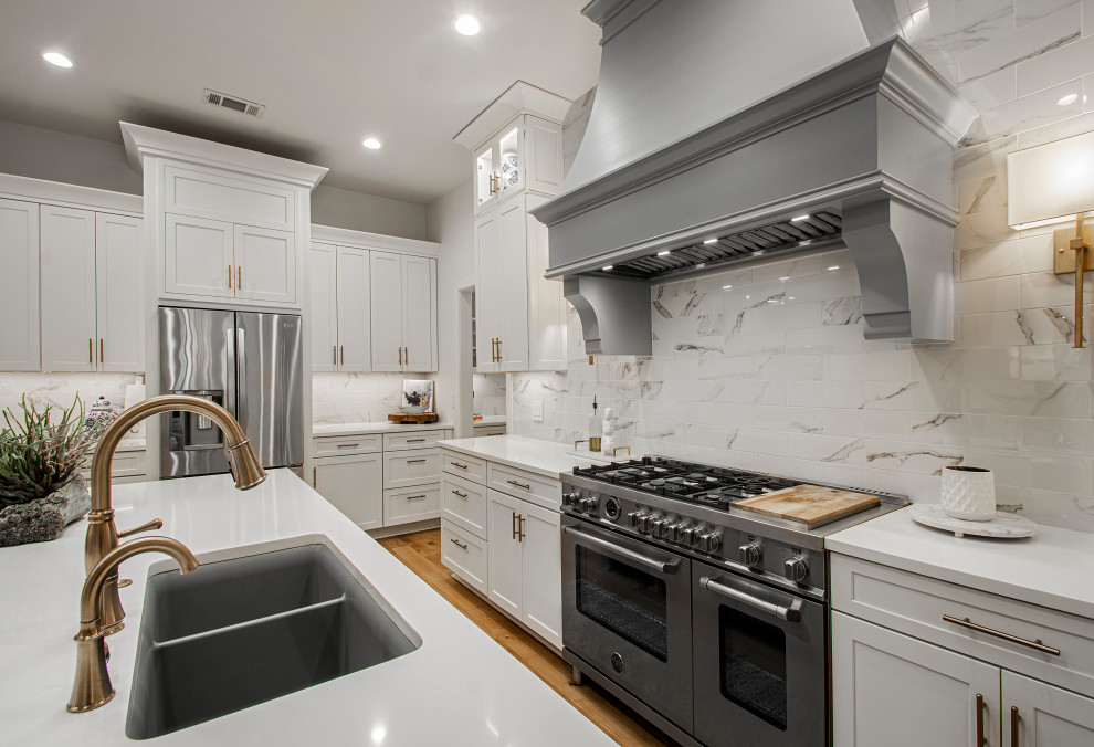 This is an example of a mid-sized transitional l-shaped kitchen in Dallas with an undermount sink, shaker cabinets, grey cabinets, white splashback, stainless steel appliances, medium hardwood floors, with island, brown floor and white benchtop.