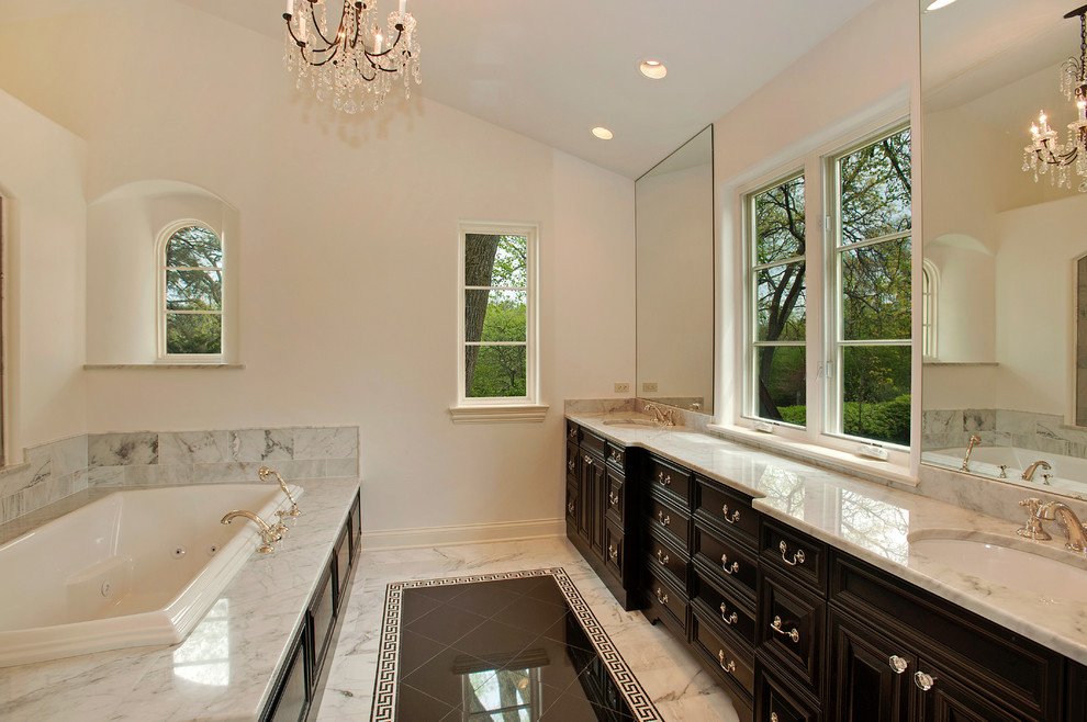 Inspiration for a large traditional master bathroom in Chicago with a drop-in tub, an undermount sink, dark wood cabinets, marble benchtops, white walls, marble floors, raised-panel cabinets and marble.