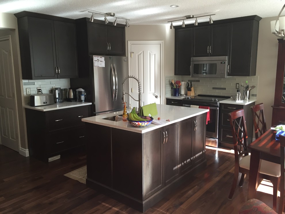 Open concept kitchen - mid-sized transitional single-wall dark wood floor and brown floor open concept kitchen idea in Calgary with a double-bowl sink, shaker cabinets, dark wood cabinets, white backsplash, subway tile backsplash, stainless steel appliances and an island
