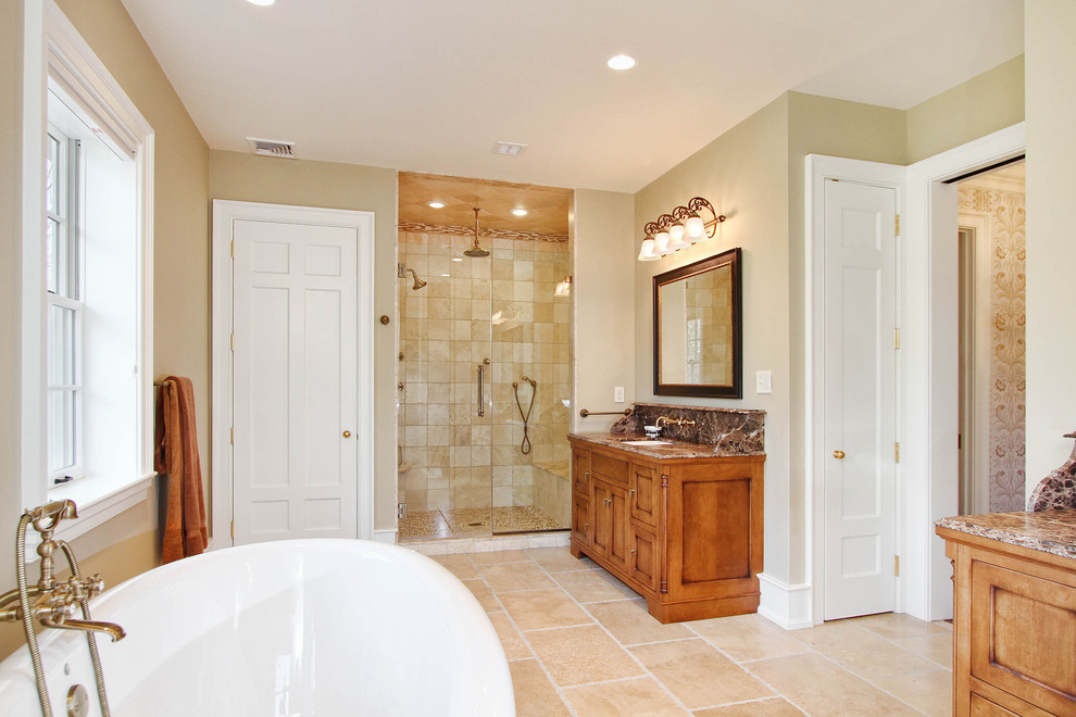 Photo of a traditional bathroom in Philadelphia with an undermount sink, recessed-panel cabinets, medium wood cabinets, granite benchtops, a freestanding tub, an alcove shower, a one-piece toilet, beige tile and beige walls.