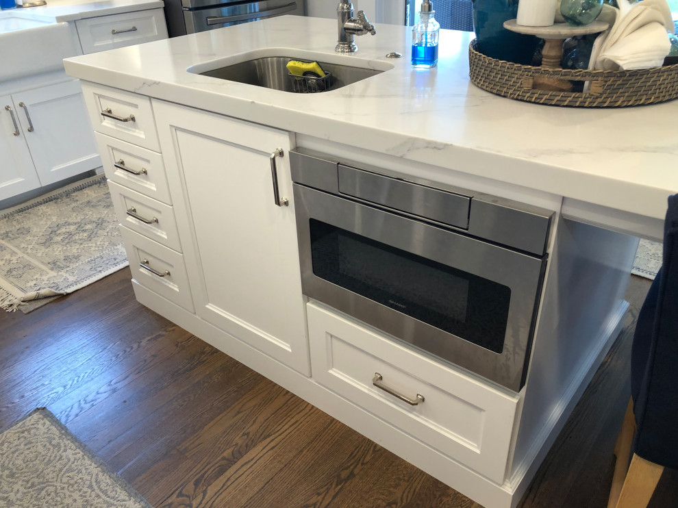 Eat-in kitchen - large transitional l-shaped medium tone wood floor and brown floor eat-in kitchen idea in Baltimore with a farmhouse sink, flat-panel cabinets, white cabinets, quartz countertops, white backsplash, subway tile backsplash, stainless steel appliances, an island and white countertops
