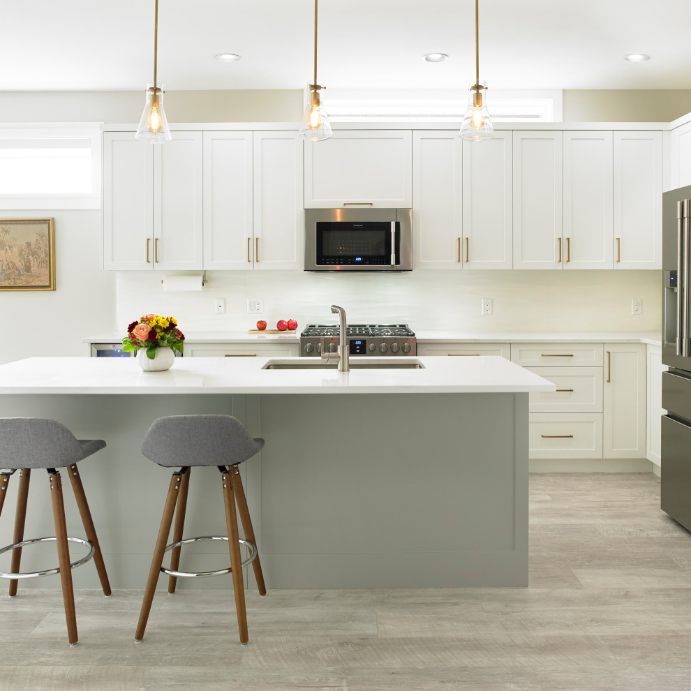 Example of a mid-sized transitional l-shaped beige floor open concept kitchen design with an undermount sink, shaker cabinets, white cabinets, quartz countertops, white backsplash, ceramic backsplash, stainless steel appliances and an island