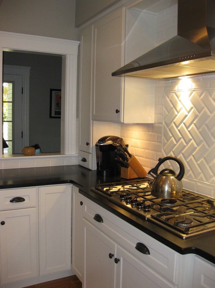 Example of a transitional l-shaped medium tone wood floor eat-in kitchen design in Boston with an undermount sink, shaker cabinets, white cabinets, granite countertops, white backsplash, ceramic backsplash, stainless steel appliances, an island and black countertops