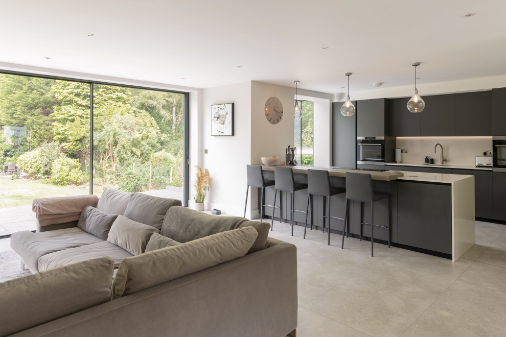 Medium sized contemporary grey and white single-wall open plan kitchen in Other with an integrated sink, flat-panel cabinets, grey cabinets, white splashback, integrated appliances, porcelain flooring, an island, beige floors and white worktops.
