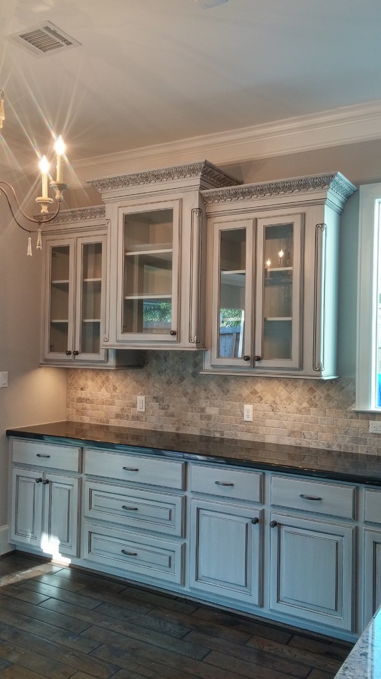 Large traditional l-shaped eat-in kitchen in Houston with an undermount sink, raised-panel cabinets, distressed cabinets, granite benchtops, beige splashback, stone tile splashback, stainless steel appliances, dark hardwood floors and with island.