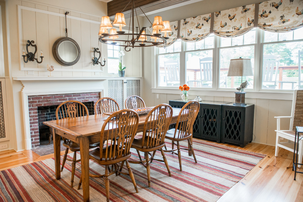 This is an example of a country dining room in Portland Maine with white walls, medium hardwood floors, a standard fireplace and a brick fireplace surround.