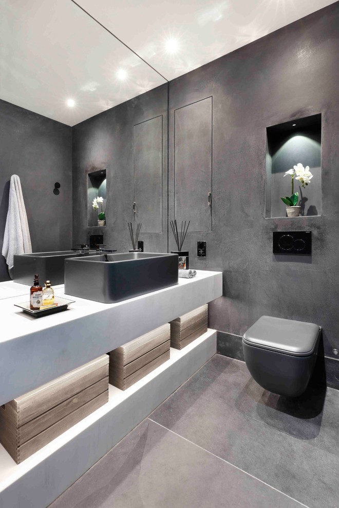 Contemporary powder room in London with black walls, slate floors, black floor, open cabinets, yellow cabinets, a wall-mount toilet, a vessel sink and white benchtops.