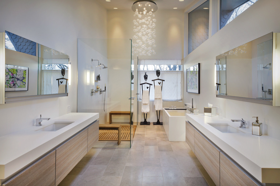 Design ideas for a large modern master bathroom in Minneapolis with an undermount sink, flat-panel cabinets, light wood cabinets, solid surface benchtops, a freestanding tub, a curbless shower, a one-piece toilet, gray tile, stone tile, white walls and limestone floors.
