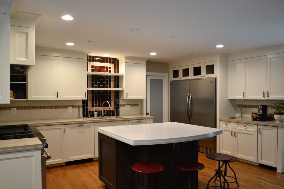Open concept kitchen - mid-sized eclectic u-shaped medium tone wood floor and brown floor open concept kitchen idea in Baltimore with an island, an undermount sink, shaker cabinets, white cabinets, solid surface countertops, white backsplash, ceramic backsplash and stainless steel appliances
