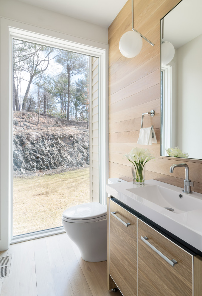This is an example of a contemporary powder room in Boston with flat-panel cabinets, light wood cabinets, white walls, light hardwood floors, an integrated sink, beige floor, white benchtops, a freestanding vanity and wood walls.