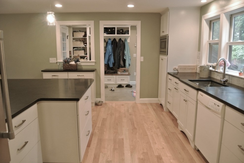 Inspiration for a transitional u-shaped light wood floor eat-in kitchen remodel in Boston with an undermount sink, shaker cabinets, white cabinets, beige backsplash, porcelain backsplash, stainless steel appliances, a peninsula and black countertops