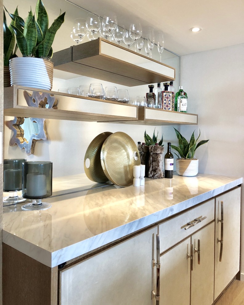 This is an example of a mid-sized modern single-wall wet bar in Miami with no sink, flat-panel cabinets, beige cabinets, marble benchtops, mirror splashback, light hardwood floors and beige floor.