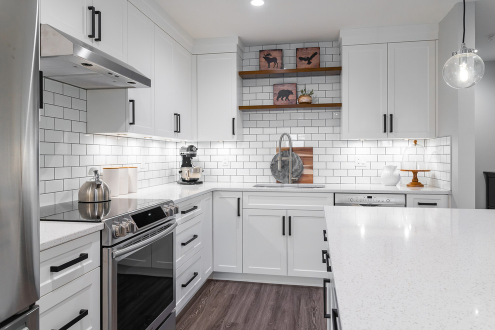 Inspiration for a mid-sized transitional l-shaped brown floor and vinyl floor eat-in kitchen remodel in Vancouver with an undermount sink, white cabinets, white backsplash, subway tile backsplash, stainless steel appliances, an island, white countertops, quartz countertops and shaker cabinets