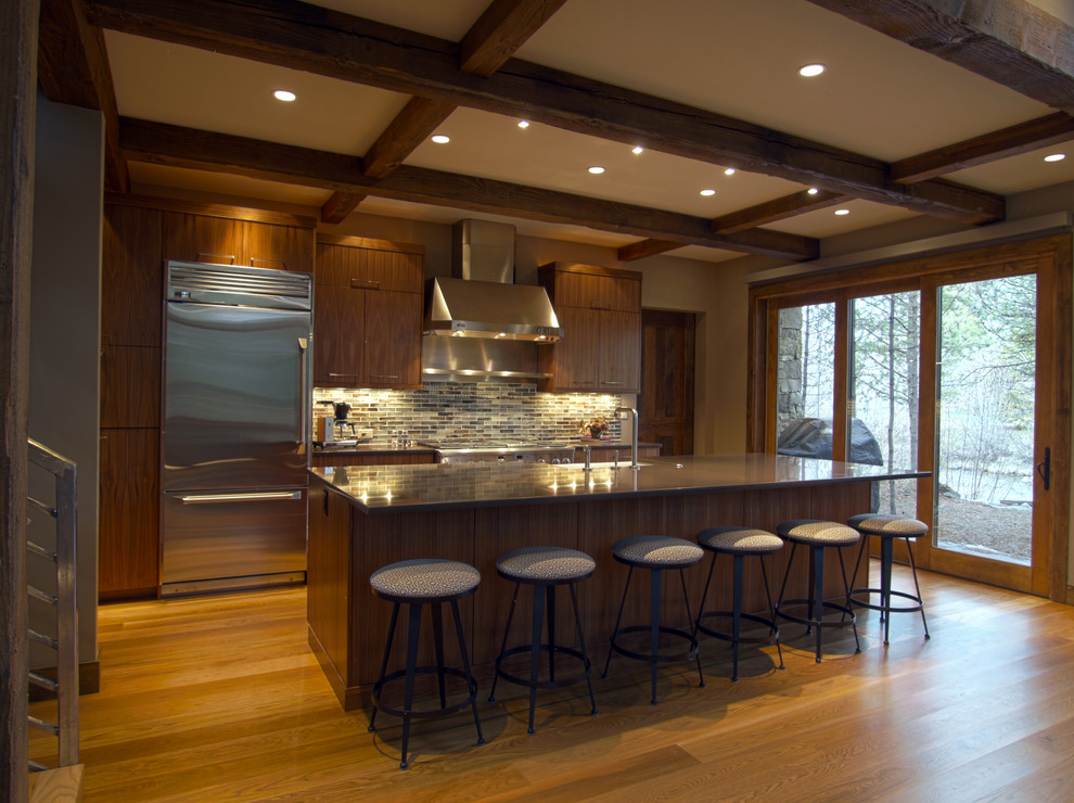 Example of a mid-sized mountain style single-wall medium tone wood floor and beige floor eat-in kitchen design in Phoenix with a farmhouse sink, flat-panel cabinets, dark wood cabinets, granite countertops, multicolored backsplash, stone tile backsplash, stainless steel appliances and an island