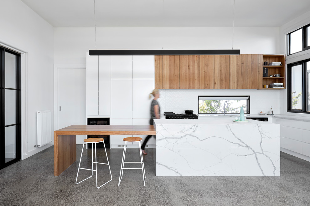 Photo of a mid-sized country l-shaped open plan kitchen in Melbourne with flat-panel cabinets, white cabinets, quartz benchtops, white splashback, marble splashback, concrete floors, with island, white benchtop, panelled appliances and grey floor.