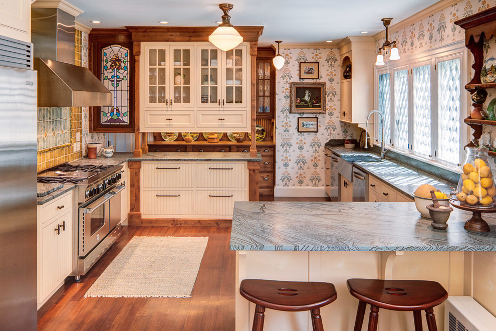 This is an example of a traditional u-shaped kitchen in Portland Maine with a farmhouse sink, flat-panel cabinets, beige cabinets, beige splashback, stainless steel appliances and blue benchtop.