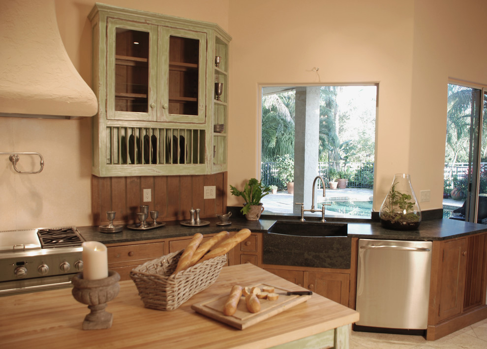 Example of a large mountain style u-shaped ceramic tile and beige floor enclosed kitchen design in Miami with a farmhouse sink, beaded inset cabinets, green cabinets, solid surface countertops, brown backsplash, wood backsplash, stainless steel appliances and an island