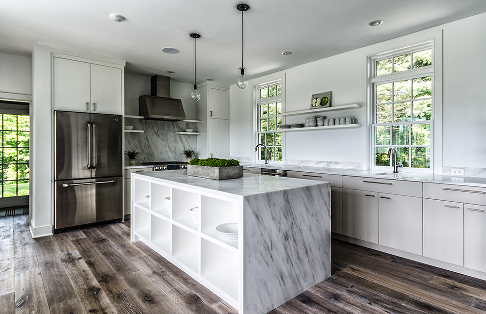 Design ideas for a mid-sized country l-shaped kitchen in New York with flat-panel cabinets, grey cabinets, marble benchtops, white splashback, stone slab splashback, stainless steel appliances, an undermount sink, light hardwood floors and with island.