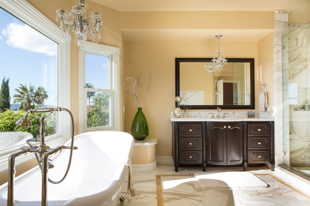 Expansive mediterranean master bathroom in Los Angeles with recessed-panel cabinets, dark wood cabinets, a claw-foot tub, a corner shower, a one-piece toilet, white tile, stone tile, beige walls, marble floors, marble benchtops and an undermount sink.