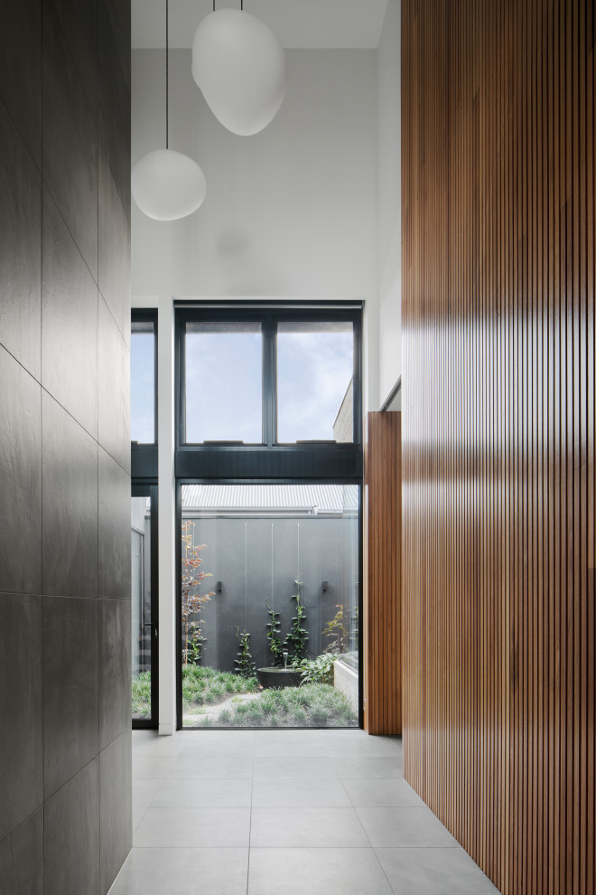 Imagen de hall minimalista grande con suelo de baldosas de porcelana, puerta pivotante, puerta de madera oscura, suelo gris y madera