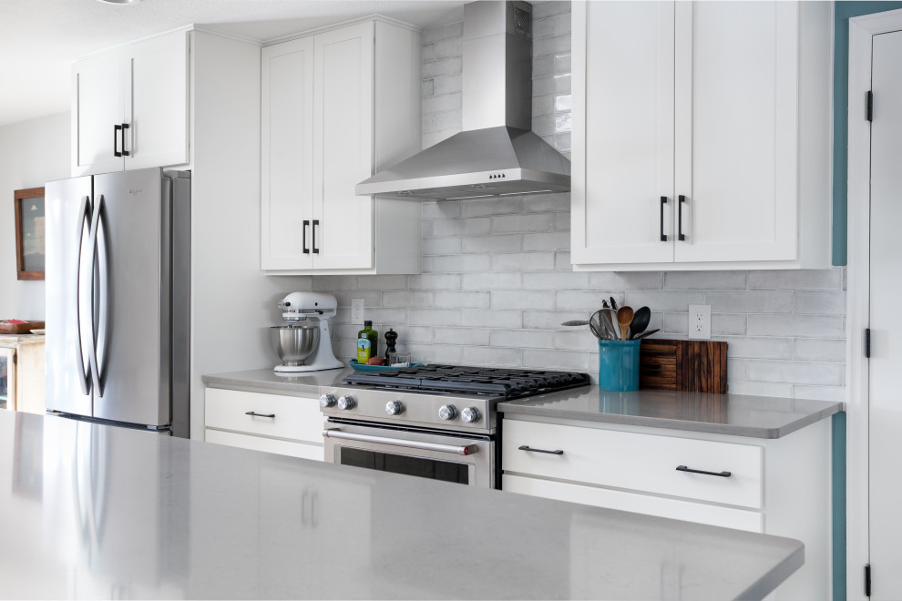 Bild på ett mellanstort vintage grå grått kök, med en undermonterad diskho, skåp i shakerstil, vita skåp, bänkskiva i kvarts, vitt stänkskydd, stänkskydd i porslinskakel, rostfria vitvaror, ljust trägolv, en köksö och brunt golv