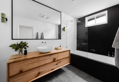 M.J. Harris Group built in bath with black penny tile and timber vanity