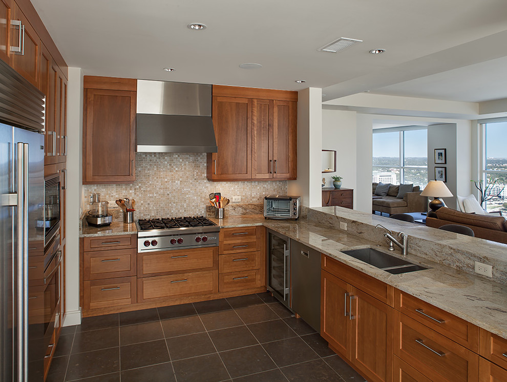 This is an example of a transitional u-shaped open plan kitchen in Austin with a double-bowl sink, recessed-panel cabinets, medium wood cabinets, granite benchtops, beige splashback, mosaic tile splashback, stainless steel appliances, porcelain floors and a peninsula.