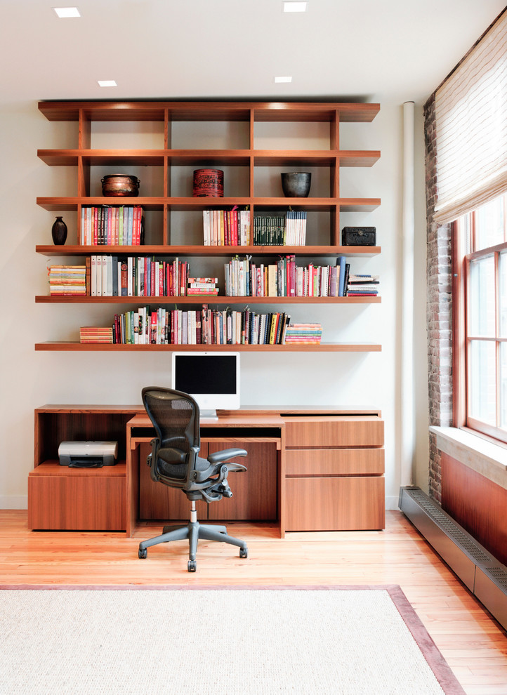 This is an example of a mid-sized contemporary home office in New York with white walls, light hardwood floors and a built-in desk.