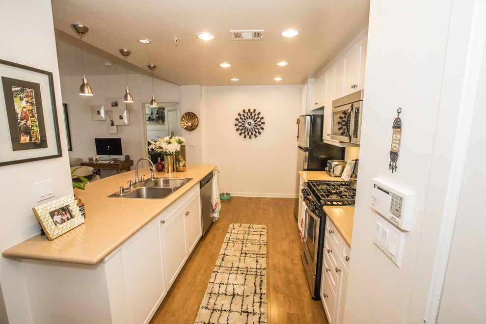 Open concept kitchen - mid-sized transitional galley dark wood floor and brown floor open concept kitchen idea in Orange County with a double-bowl sink, shaker cabinets, white cabinets, solid surface countertops, a peninsula and stainless steel appliances