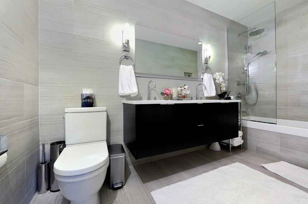 Design ideas for a mid-sized contemporary bathroom in New York with an integrated sink, flat-panel cabinets, black cabinets, solid surface benchtops, an alcove tub, a shower/bathtub combo, a two-piece toilet, gray tile and beige walls.