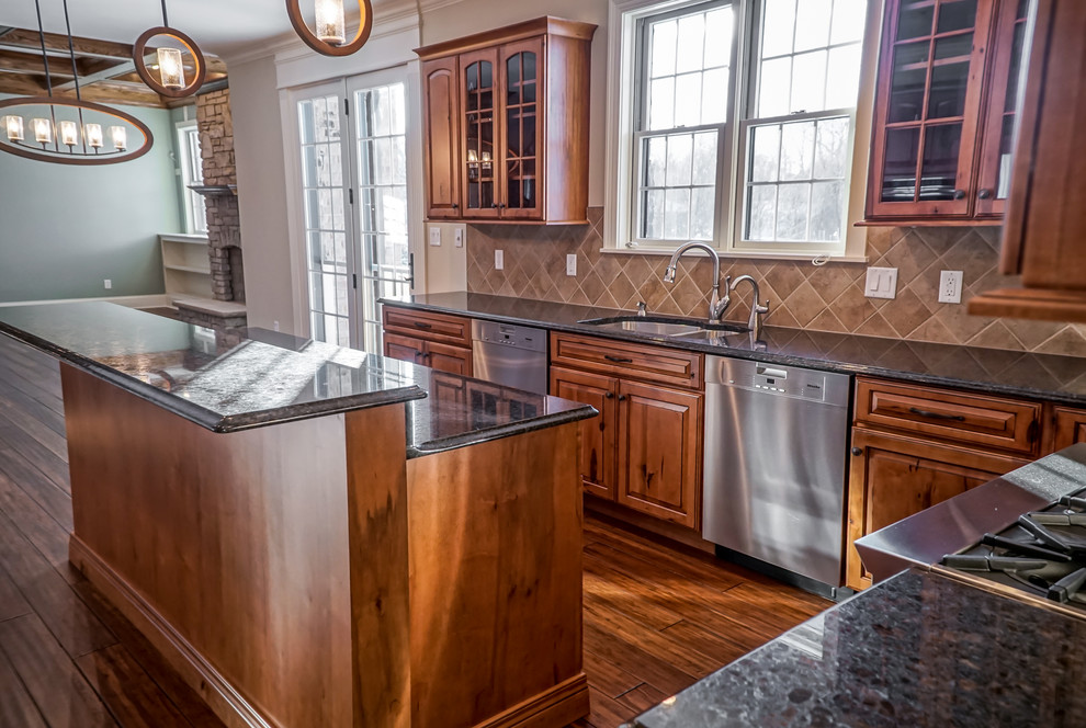 Example of a mid-sized mountain style u-shaped medium tone wood floor eat-in kitchen design in Chicago with an undermount sink, raised-panel cabinets, distressed cabinets, granite countertops, beige backsplash, stone tile backsplash, stainless steel appliances and an island