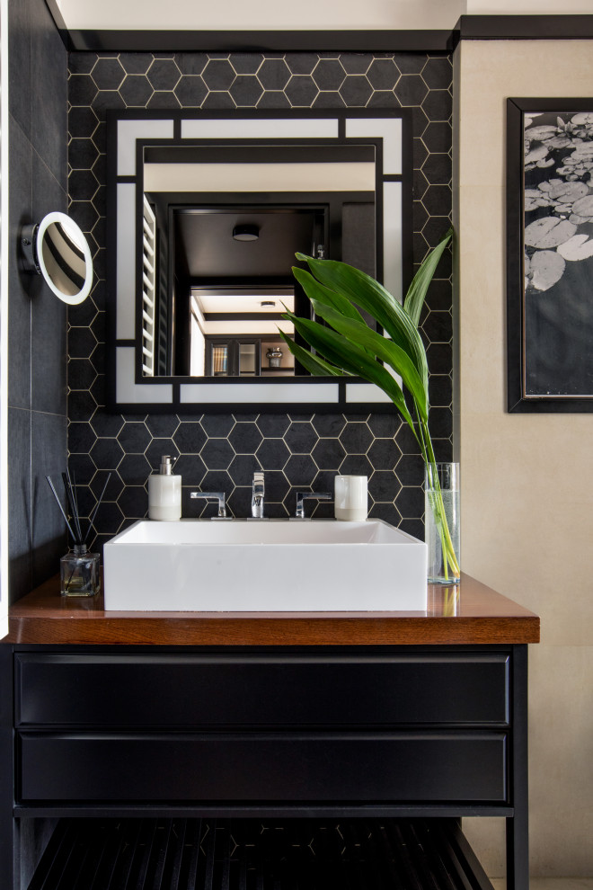 Пример оригинального дизайна: маленькая серо-белая ванная комната в стиле неоклассика (современная классика) с фасадами с выступающей филенкой, черными фасадами, душем в нише, инсталляцией, черно-белой плиткой, керамической плиткой, полом из керамической плитки, душевой кабиной, накладной раковиной, столешницей из дерева, черным полом, душем с распашными дверями, коричневой столешницей, гигиеническим душем, тумбой под одну раковину и встроенной тумбой для на участке и в саду
