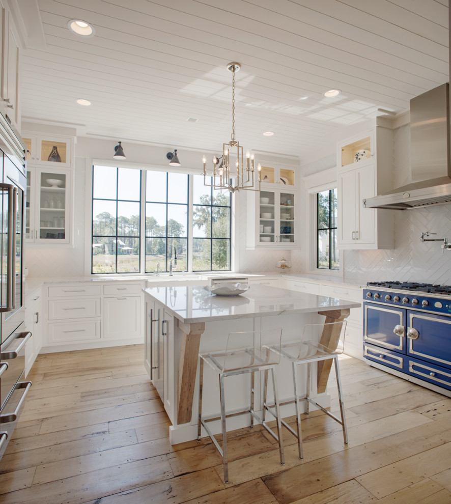 Beach style u-shaped kitchen in Atlanta with a farmhouse sink, shaker cabinets, white cabinets, white splashback, coloured appliances, light hardwood floors, with island, white benchtop and timber.