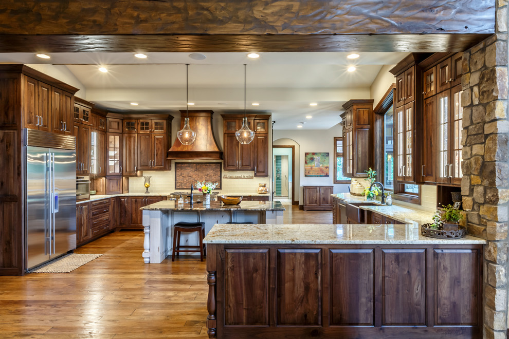 Huge mountain style medium tone wood floor eat-in kitchen photo in Denver with a farmhouse sink, raised-panel cabinets, dark wood cabinets, beige backsplash, stainless steel appliances and an island