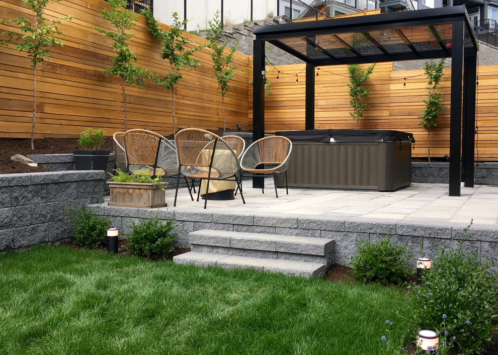 Medium sized modern sloped full sun garden for spring in Vancouver with concrete paving, a wood fence and a retaining wall.