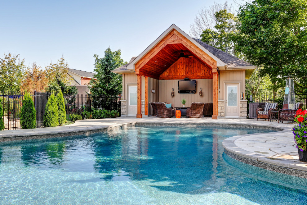 Large transitional backyard custom-shaped pool in Toronto with a pool house and stamped concrete.