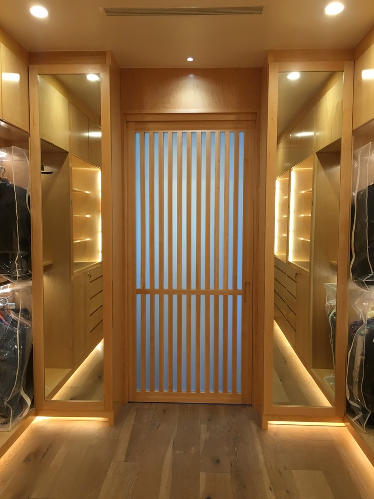 Photo of an expansive contemporary gender-neutral walk-in wardrobe in Los Angeles with flat-panel cabinets, light wood cabinets and light hardwood floors.