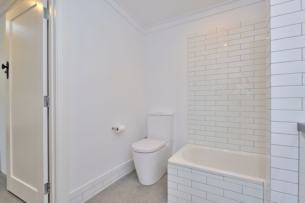 This is an example of a mid-sized modern kids bathroom in Perth with flat-panel cabinets, white cabinets, a drop-in tub, a shower/bathtub combo, a two-piece toilet, white tile, subway tile, white walls, concrete floors, a vessel sink, concrete benchtops, grey floor, an open shower and grey benchtops.