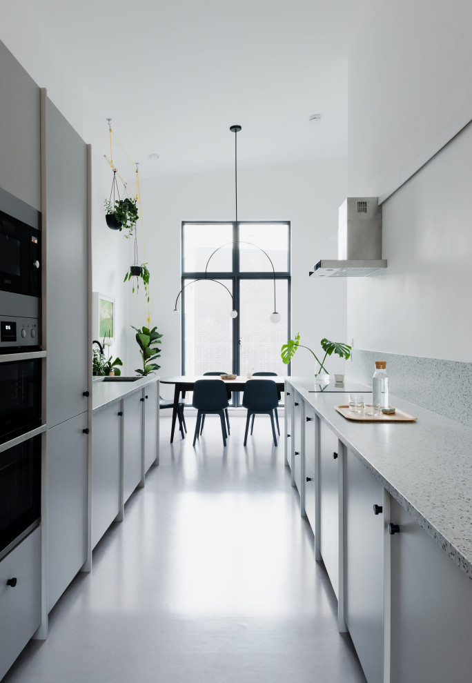 Photo of a large contemporary galley kitchen/diner in London with a built-in sink, flat-panel cabinets, grey cabinets, terrazzo worktops, black appliances, no island and a vaulted ceiling.