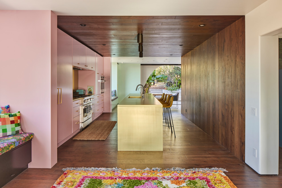 Photo of a large mediterranean single-wall open plan kitchen in Los Angeles with a submerged sink, flat-panel cabinets, pink cabinets, yellow splashback, metal splashback, stainless steel appliances, dark hardwood flooring, an island, yellow worktops, a wood ceiling and brown floors.