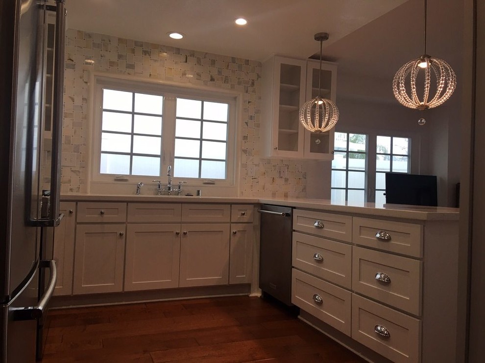 Inspiration for a mid-sized transitional u-shaped medium tone wood floor and brown floor open concept kitchen remodel in Los Angeles with an undermount sink, recessed-panel cabinets, white cabinets, quartz countertops, white backsplash, ceramic backsplash, stainless steel appliances, a peninsula and white countertops